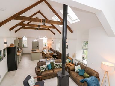 An open living room and kitchen with wooden beams on the ceiling and a black stove in the center at Ysgoldy Brynwyre in Llanrhystud