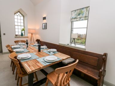 A dining area with a wooden table set with plates glasses and bottles surrounded by wooden chairs and a wooden bench at Ysgoldy Brynwyre in Llanrhystud