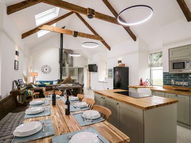 A kitchen and dining area with wooden table set for six and an island with stove under wooden beams at Ysgoldy Brynwyre in Llanrhystud