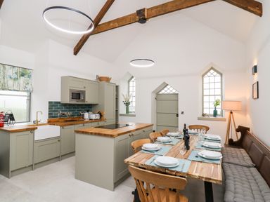 A kitchen and dining area with wooden dining table set with plates and glasses and a kitchen island at Ysgoldy Brynwyre in Llanrhystud