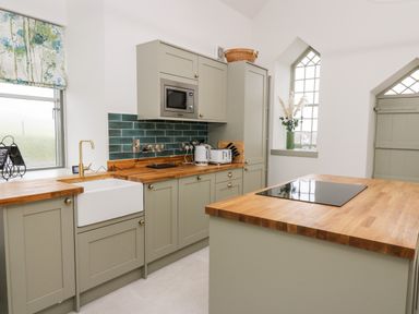 A kitchen with green cabinets wooden countertops a white farmhouse sink and a microwave at Ysgoldy Brynwyre in Llanrhystud