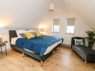 A bedroom with a double bed side tables lamps and a chaise lounge with cushions at Ysgoldy Brynwyre in Llanrhystud