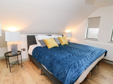 A bedroom with a bed covered in a blue quilt and pillows with two bedside tables with lamps at Ysgoldy Brynwyre in Llanrhystud