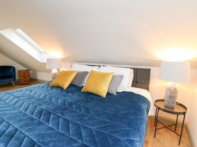 A bedroom with a bed with blue blanket and pillows a side table with lamp and a blue chair in the corner at Ysgoldy Brynwyre in Llanrhystud