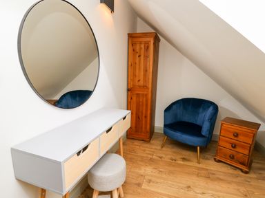 A room with a white desk with drawers a round mirror a gray stool a blue armchair a wooden cabinet and a wooden drawer unit at Ysgoldy Brynwyre in Llanrhystud