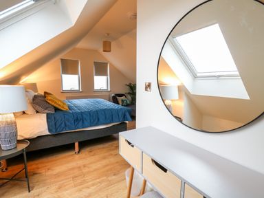 A bedroom with a bed with blue bedding a side table with a lamp a round mirror and a desk with drawers at Ysgoldy Brynwyre in Llanrhystud