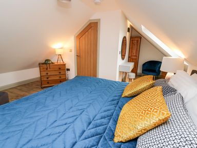 A bedroom with a blue bedspread yellow pillows wooden drawers a round mirror and a blue chair at Ysgoldy Brynwyre in Llanrhystud