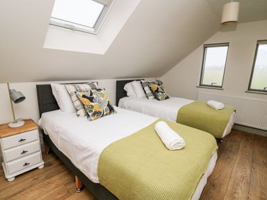 A bedroom with two single beds green throws pillows a nightstand lamp and skylight window at Ysgoldy Brynwyre in Llanrhystud