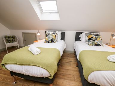 A bedroom with two single beds with green blankets and patterned pillows two bedside tables with lamps a wicker chair and a skylight window at Ysgoldy Brynwyre in Llanrhystud