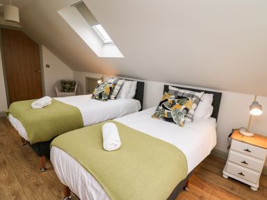 A bedroom with two single beds green blankets and rolled white towels at Ysgoldy Brynwyre in Llanrhystud