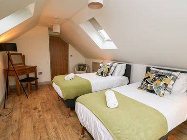 A bedroom with two single beds with green throws and decorative pillows a wooden dressing table with stool and lamp on wooden floor at Ysgoldy Brynwyre in Llanrhystud