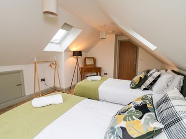 A bedroom with two single beds pillows and blankets a wooden door a lamp and a skylight at Ysgoldy Brynwyre in Llanrhystud