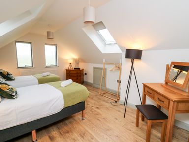 A bedroom with two single beds a wooden dressing table with mirror a coat rack and two windows at Ysgoldy Brynwyre in Llanrhystud