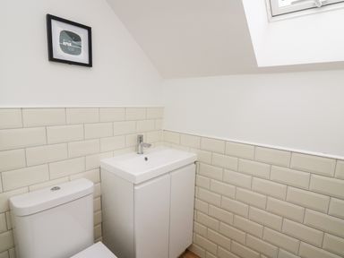 A bathroom with a toilet a sink with cabinet tiles on the wall and a framed picture at Ysgoldy Brynwyre in Llanrhystud