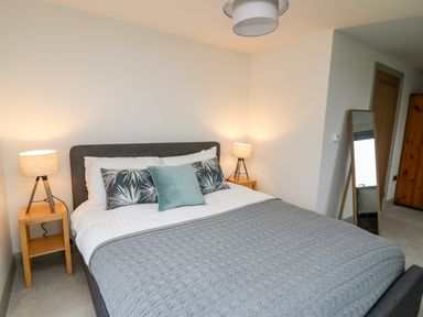A bedroom with a bed a gray knitted blanket two bedside tables with lamps a standing mirror and a wooden wardrobe at Ysgoldy Brynwyre Llanrhystud