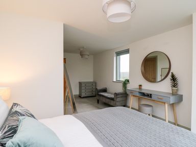 A bedroom with a bed a dressing table with a round mirror a stool a gray bench and a chest of drawers at Ysgoldy Brynwyre Llanrhystud