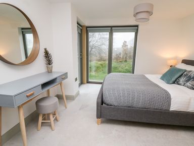 A bedroom with a gray bed a gray desk with a round mirror and a stool near large windows at Ysgoldy Brynwyre in Llanrhystud