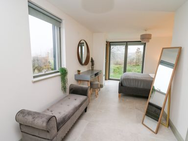 A bedroom with a bench, dressing table, round mirror, and floor mirror at Ysgoldy Brynwyre in Llanrhystud