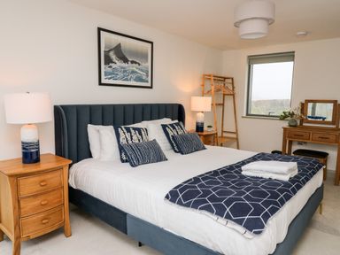 A bedroom with a bed, two bedside tables with lamps, a wooden clothes rack, a window, and a wooden dressing table with a mirror at Ysgoldy Brynwyre in Llanrhystud