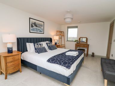 A bedroom with a double bed blue headboard bedside tables lamps a wooden dressing table and a window at Ysgoldy Brynwyre in Llanrhystud