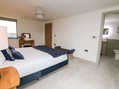 A bedroom with a bed, a wooden dresser with a mirror, a bench, and an ensuite bathroom at Ysgoldy Brynwyre in Llanrhystud