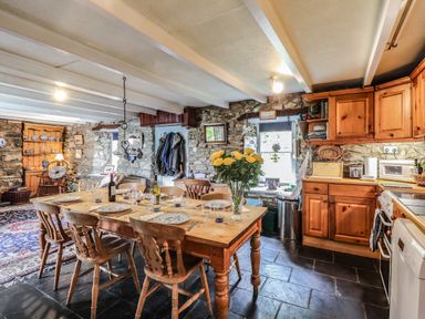 A kitchen dining area with wooden table and chairs stone walls wooden cabinets and a bouquet of yellow flowers at Tyddyn Bach Newport Pembrokeshire