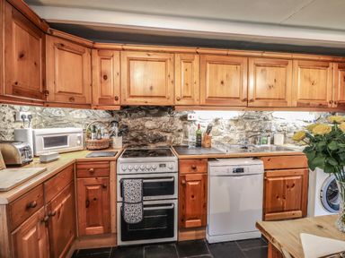 A kitchen with wooden cabinets stone wall oven dishwasher and flowers on a table at Tyddyn Bach in Newport Pembrokeshire