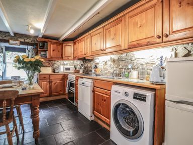 A kitchen with wooden cabinets a dining table with flowers on it and appliances at Tyddyn Bach in Newport Pembrokeshire