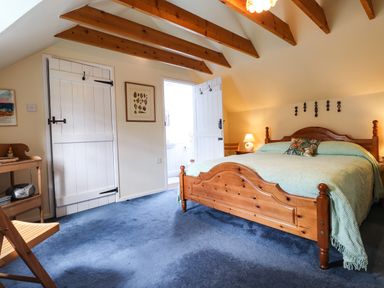 A bedroom with a wooden bed with a green bedspread and exposed ceiling beams at Tyddyn Bach in Newport Pembrokeshire