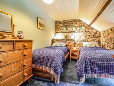 A bedroom with two single beds stone walls wooden dresser and bedside table at Tyddyn Bach in Newport Pembrokeshire