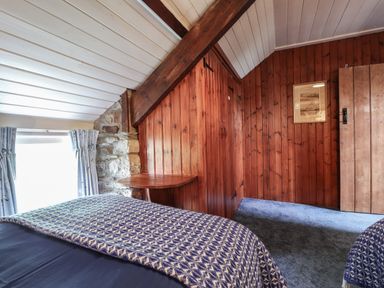 A bedroom with blue patterned blankets a wooden wardrobe stone wall section and window with curtains at Tyddyn Bach in Newport Pembrokeshire