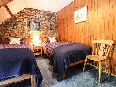 A bedroom with two single beds a wooden chair and a stone wall at Tyddyn Bach in Newport Pembrokeshire