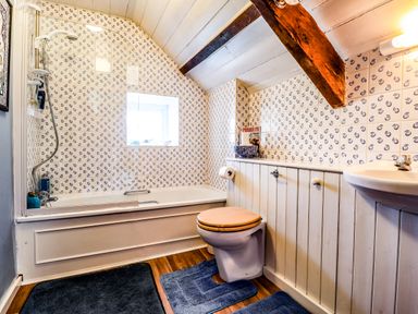A bathroom with bathtub shower toilet with wooden seat and sink with blue mats on the floor at Tyddyn Bach Newport Pembrokeshire