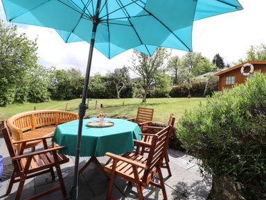 An outdoor patio with wooden chairs a table with a teal tablecloth and umbrella in a garden at Tyddyn Bach Newport Pembrokeshire