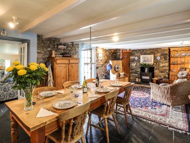 A dining area with a wooden table set with plates and glasses and a seating area with wicker and wooden furniture at Tyddyn Bach in Newport Pembrokeshire