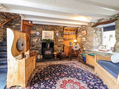 A living room with stone walls wooden furniture a fireplace and a patterned rug at Tyddyn Bach in Newport Pembrokeshire