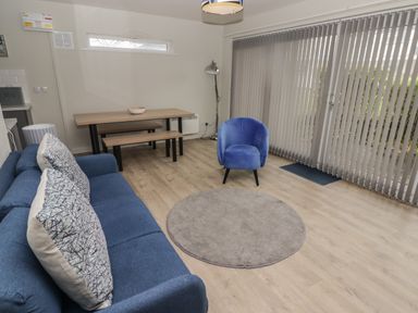 A living room with a blue sofa and chair a wooden dining table with benches and vertical blinds at 21 Coedrath Park in Saundersfoot