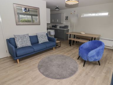 A living room with a blue sofa a blue armchair a round gray rug a wooden dining table with benches and a wall mirror at 21 Coedrath Park Saundersfoot