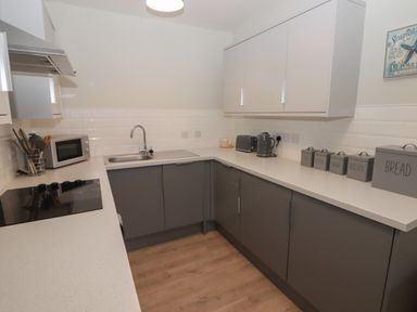 A kitchen with grey lower cabinets white upper cabinets a sink a microwave toaster kettle and labeled containers at 21 Coedrath Park in Saundersfoot