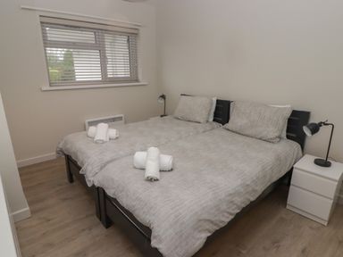 A bedroom with two single beds side by side with gray bedding pillows rolled towels bedside table with lamp and window with blinds at 21 Coedrath Park Saundersfoot