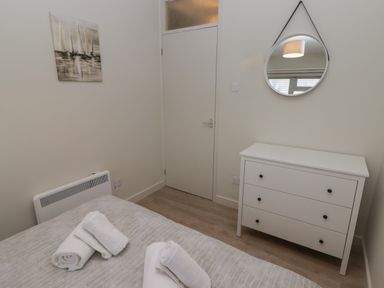 A bedroom with a bed with rolled towels on it a white door a white dresser with three drawers and a round mirror above at 21 Coedrath Park in Saundersfoot