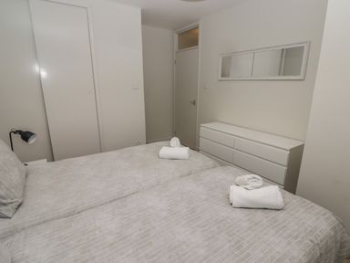A bedroom with two beds a white dresser a wall mirror and a closed door at 21 Coedrath Park in Saundersfoot