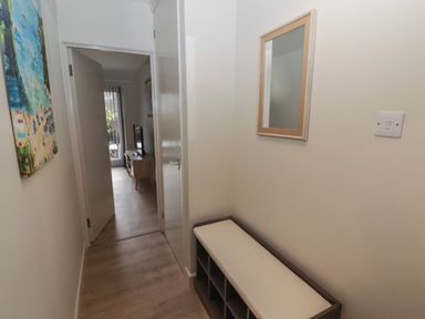 A hallway with a bench and cubby storage a wall mirror and a painting a door leading to a room with a TV stand and television at 21 Coedrath Park in Saundersfoot