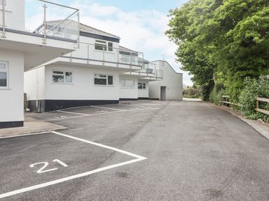 A parking area with marked spaces next to a white building with balconies and trees on the side at 21 Coedrath Park Saundersfoot