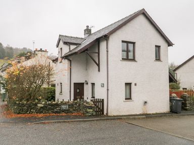A white two-story house with a stone wall and tree on the side with a sign saying Abbots Vue at Friars Fold in Newby Bridge