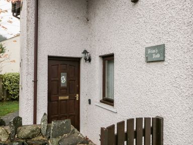 An exterior view of a house entrance with a brown door a window a stone wall a wooden gate and a sign that reads Friars Fold in Newby Bridge