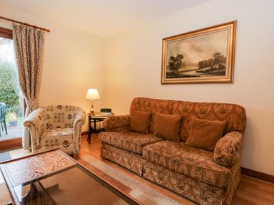 A living room with a patterned sofa a floral armchair a lamp on a side table and a landscape painting at Friars Fold in Newby Bridge