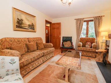 A living room with patterned sofas a wooden coffee table a painting on the wall and a window with curtains at Friars Fold in Newby Bridge