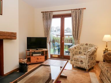 A living room with a television on a wooden stand a patterned armchair and glass coffee table at Friars Fold in Newby Bridge
