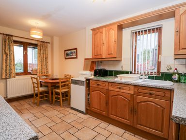 A kitchen with wooden cabinets a dining table with chairs and windows with curtains at Friars Fold in Newby Bridge